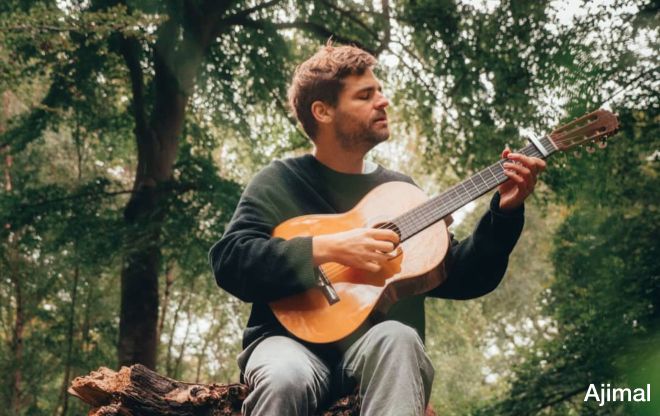 Ajimal playing guitar while sitting on a branch in the forest